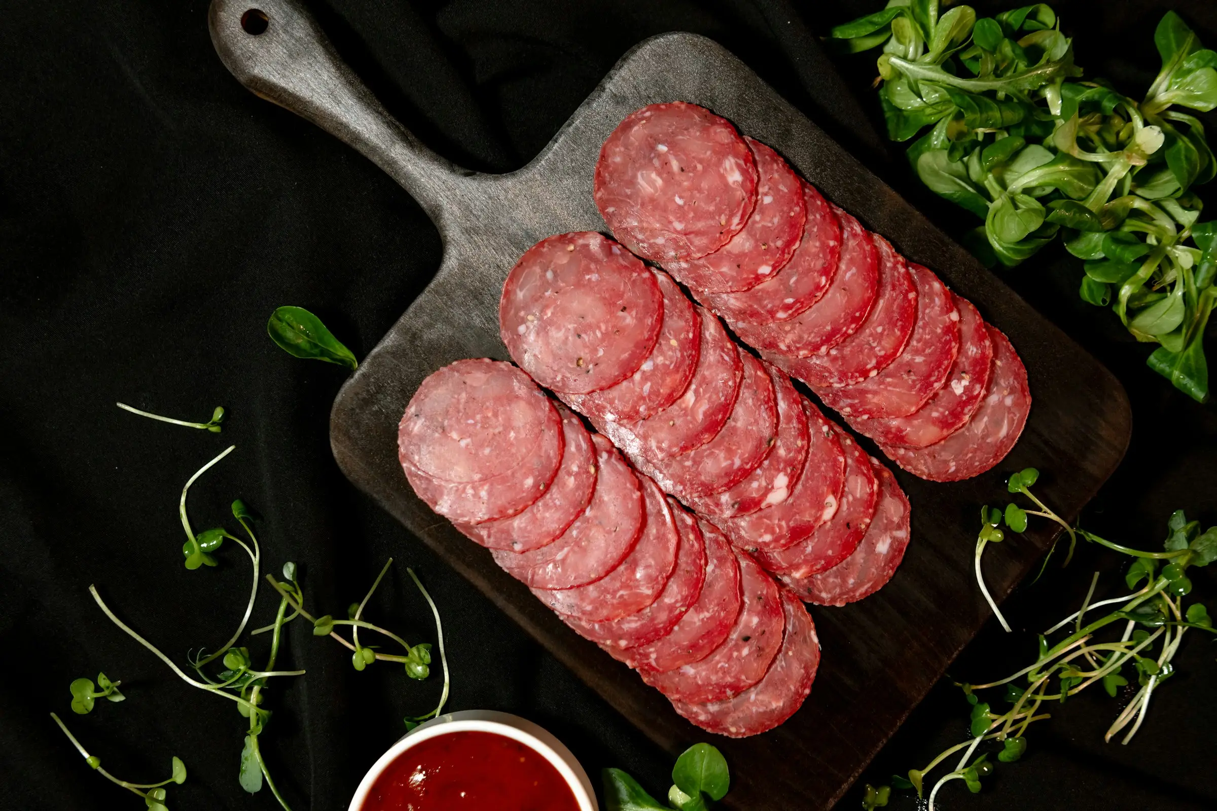 Saucisson sec tranché sur une planche, sur fond sombre
